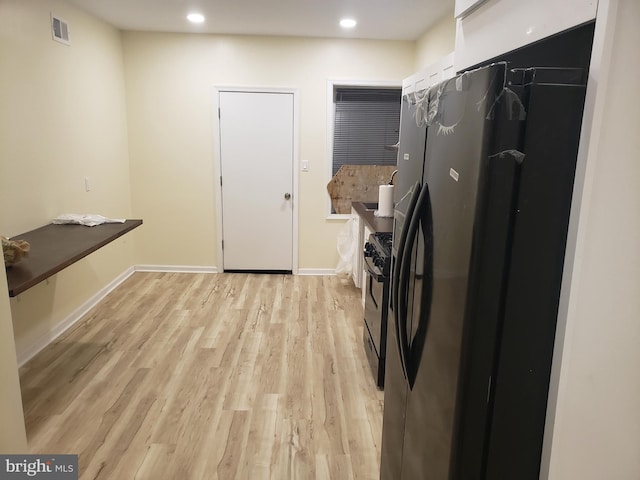 kitchen featuring white cabinets, black refrigerator, light hardwood / wood-style flooring, and gas range