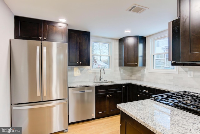 kitchen with light stone counters, dark brown cabinetry, sink, and appliances with stainless steel finishes