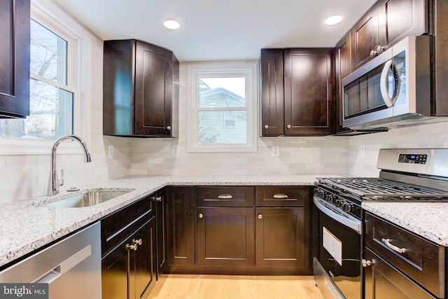 kitchen featuring appliances with stainless steel finishes, tasteful backsplash, light stone counters, dark brown cabinets, and sink