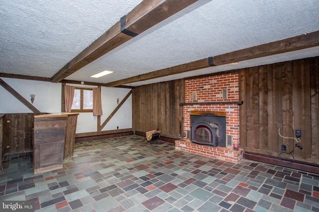 unfurnished living room featuring a wood stove, wooden walls, beamed ceiling, and a textured ceiling