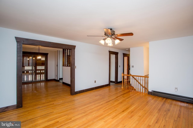 spare room with light wood-type flooring, ceiling fan with notable chandelier, and a baseboard heating unit