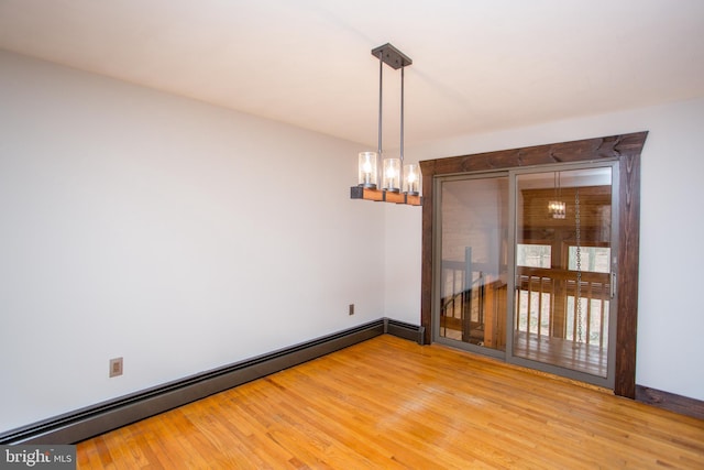 spare room featuring baseboard heating, hardwood / wood-style floors, and a chandelier