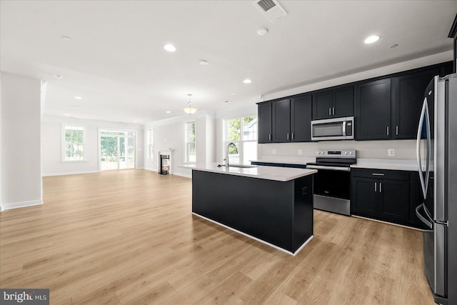 kitchen with appliances with stainless steel finishes, light wood-type flooring, a kitchen island with sink, sink, and hanging light fixtures