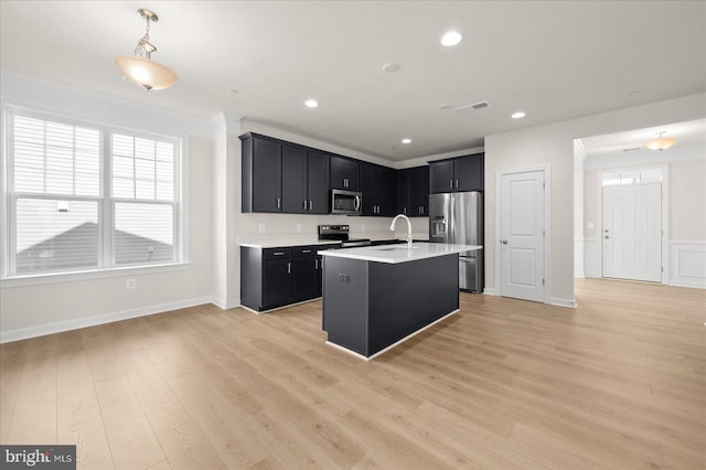 kitchen with a kitchen island with sink, sink, light wood-type flooring, and appliances with stainless steel finishes