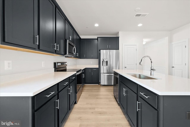 kitchen featuring a kitchen island with sink, sink, light wood-type flooring, and appliances with stainless steel finishes