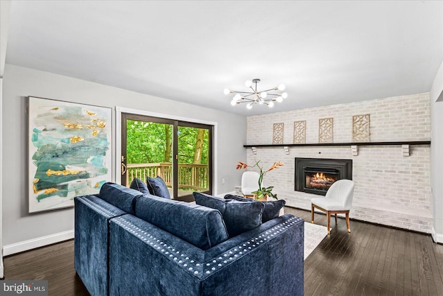 living room with a chandelier, dark wood-type flooring, brick wall, and a brick fireplace