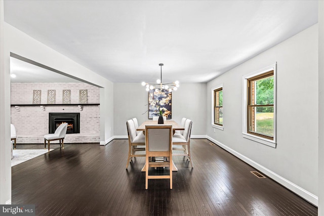 dining room featuring dark hardwood / wood-style flooring, a notable chandelier, and a brick fireplace