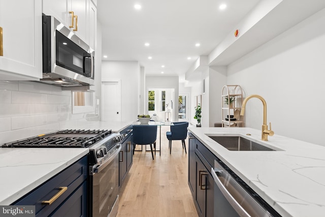 kitchen featuring sink, stainless steel appliances, light stone counters, light hardwood / wood-style floors, and white cabinets