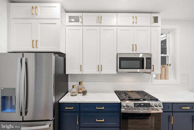 kitchen with light stone countertops, stainless steel appliances, blue cabinets, backsplash, and white cabinets