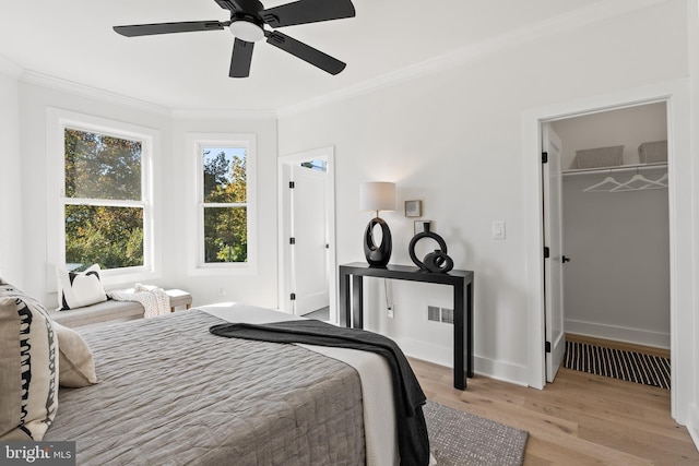 bedroom with a walk in closet, ornamental molding, ceiling fan, light hardwood / wood-style floors, and a closet