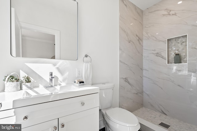 bathroom featuring a tile shower, vanity, and toilet