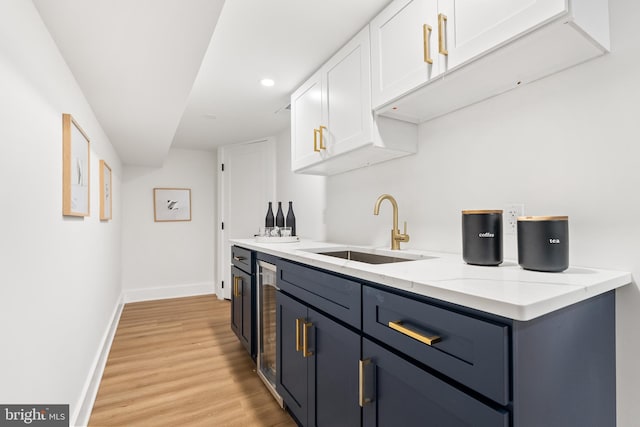 kitchen featuring white cabinetry, sink, light stone countertops, and light wood-type flooring