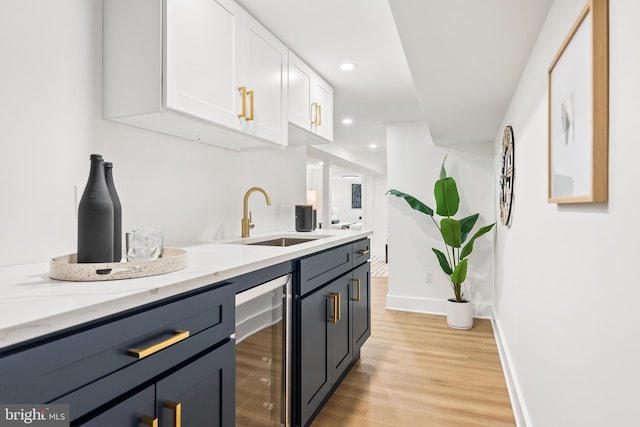 bar featuring light stone counters, sink, white cabinets, light hardwood / wood-style floors, and wine cooler