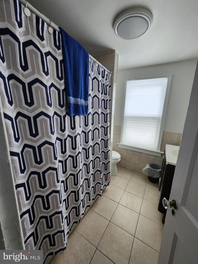 bathroom with curtained shower, tile patterned floors, toilet, vanity, and tile walls