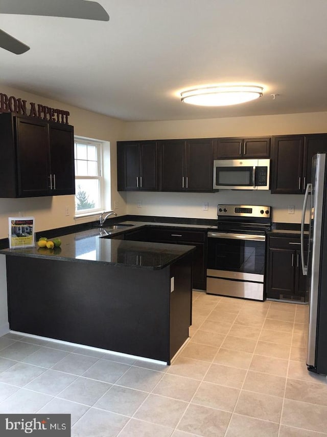 kitchen with light tile patterned flooring, dark stone countertops, sink, and appliances with stainless steel finishes