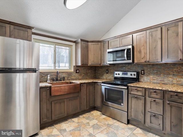 kitchen featuring light stone countertops, decorative backsplash, stainless steel appliances, vaulted ceiling, and sink