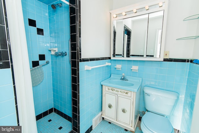 bathroom featuring tile patterned flooring, toilet, tiled shower, vanity, and tile walls