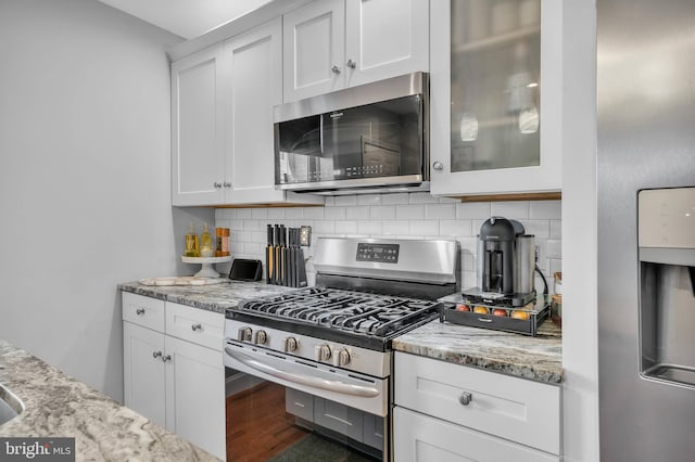 kitchen with tasteful backsplash, light stone countertops, white cabinets, and appliances with stainless steel finishes