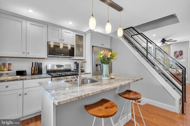 kitchen featuring light stone countertops, backsplash, stainless steel appliances, ceiling fan, and pendant lighting