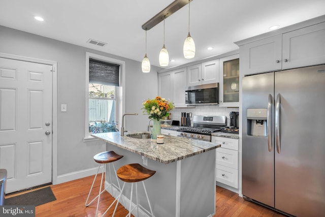 kitchen with stainless steel appliances, light stone counters, backsplash, a breakfast bar, and white cabinets