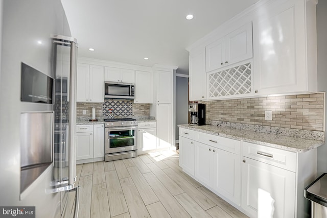 kitchen with light stone countertops, white cabinets, stainless steel appliances, decorative backsplash, and crown molding