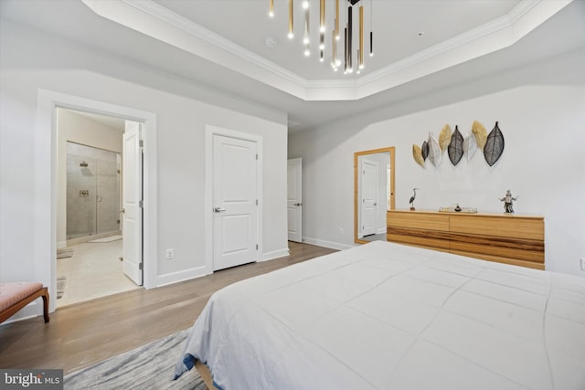 bedroom featuring connected bathroom, an inviting chandelier, crown molding, hardwood / wood-style floors, and a tray ceiling