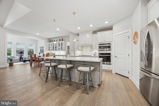 kitchen with stainless steel appliances, an island with sink, pendant lighting, a kitchen bar, and white cabinets