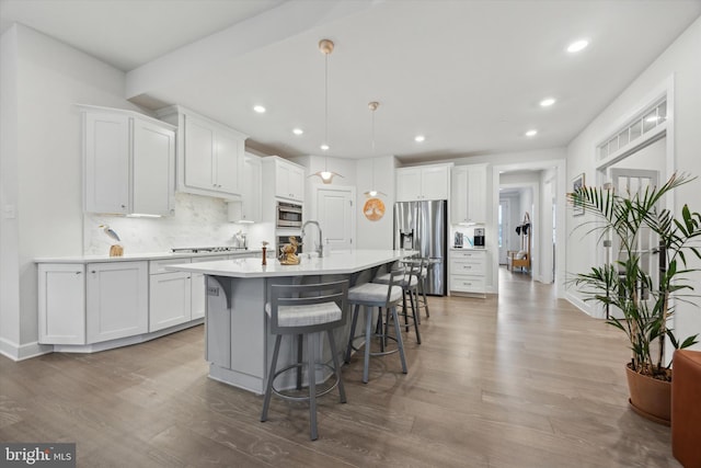 kitchen with hanging light fixtures, stainless steel appliances, backsplash, a center island with sink, and white cabinets