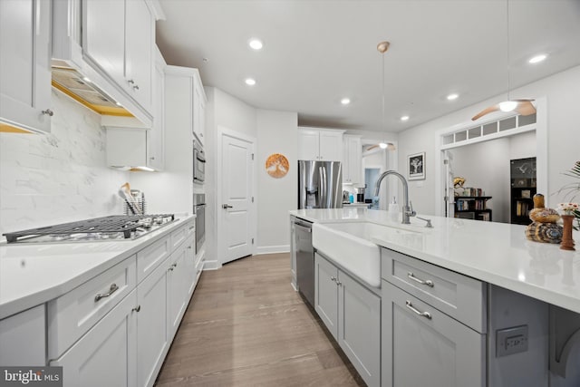 kitchen with sink, hanging light fixtures, backsplash, light hardwood / wood-style floors, and appliances with stainless steel finishes