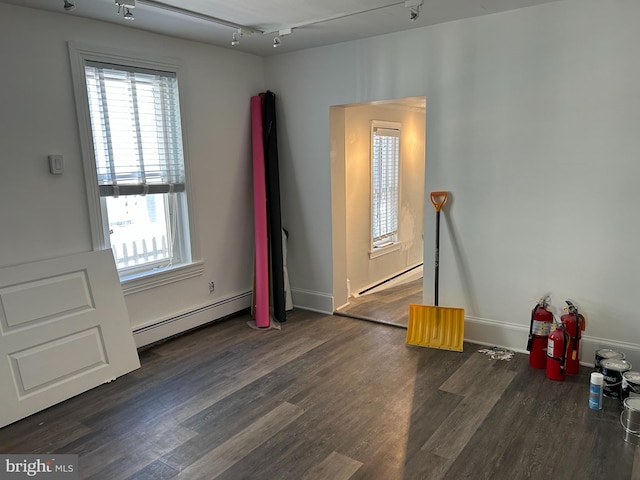 unfurnished room with dark wood-type flooring, track lighting, and a baseboard heating unit