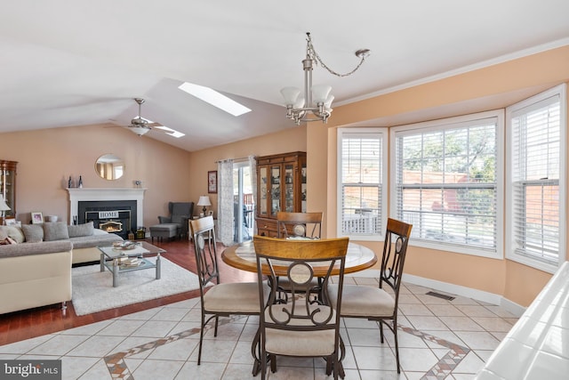 dining area with ceiling fan with notable chandelier, vaulted ceiling with skylight, light tile patterned floors, and ornamental molding