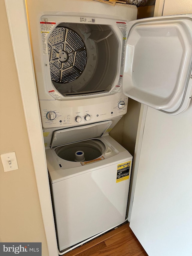 laundry room featuring stacked washer and dryer and dark wood-type flooring