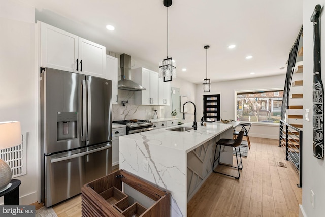 kitchen featuring white cabinets, sink, wall chimney exhaust hood, light stone counters, and stainless steel appliances