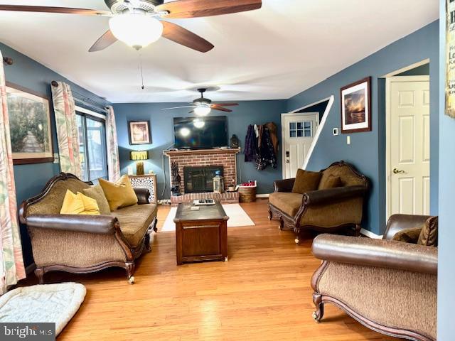 living room featuring ceiling fan, light hardwood / wood-style floors, and a brick fireplace