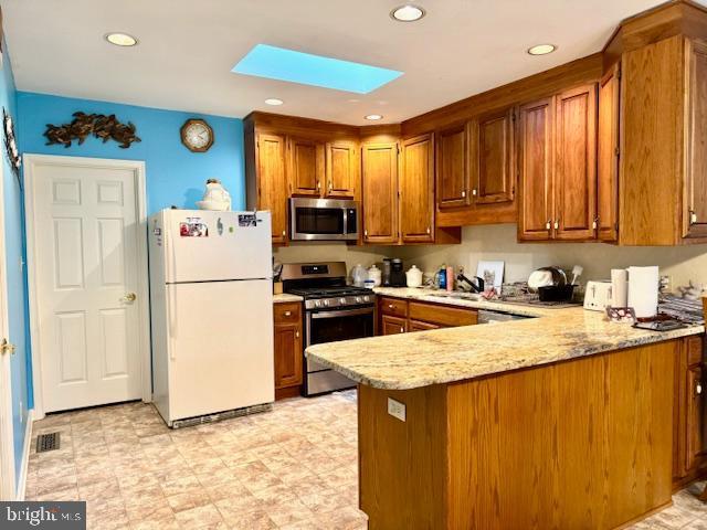 kitchen with sink, a skylight, light stone countertops, kitchen peninsula, and stainless steel appliances