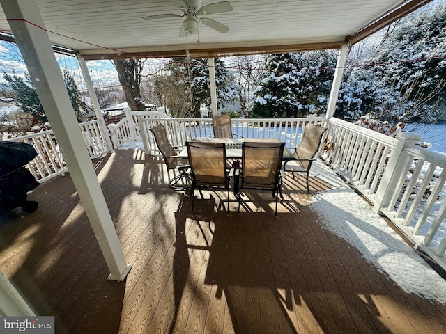 snow covered deck with outdoor dining space and ceiling fan