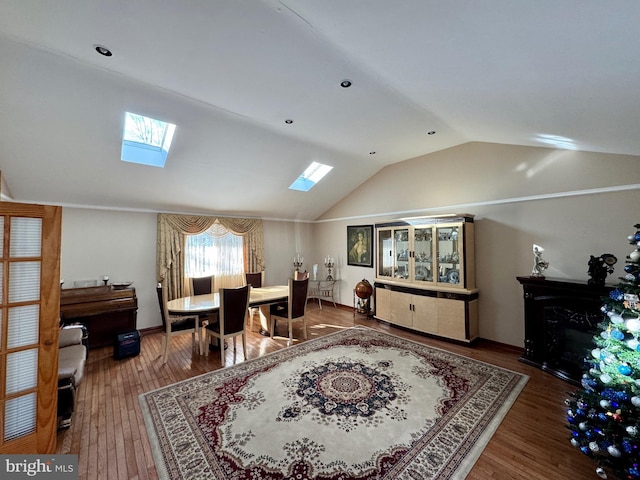 dining area with a glass covered fireplace, lofted ceiling with skylight, and wood finished floors