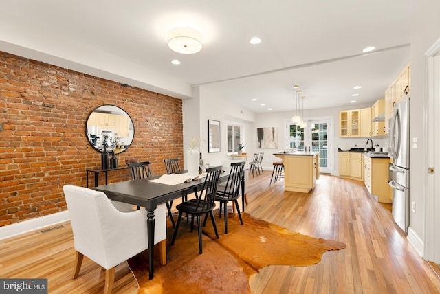 dining space with light wood-type flooring and brick wall