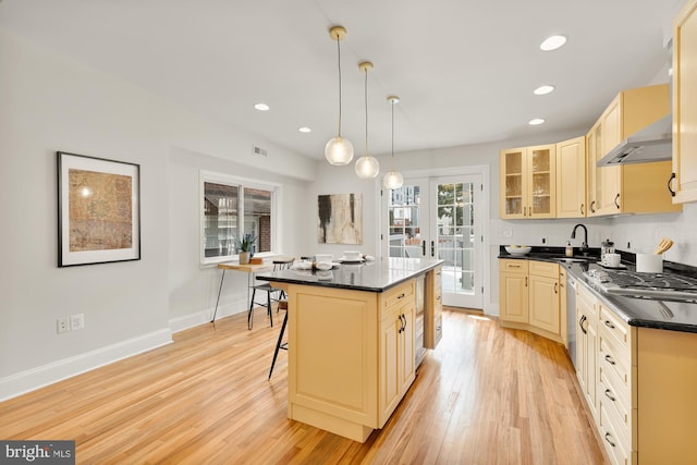 kitchen with a kitchen bar, light wood-type flooring, sink, a kitchen island, and hanging light fixtures