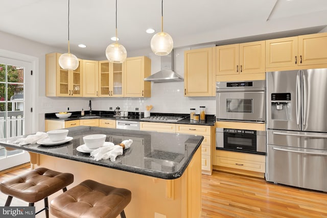 kitchen with a center island, wall chimney exhaust hood, decorative light fixtures, a breakfast bar, and appliances with stainless steel finishes