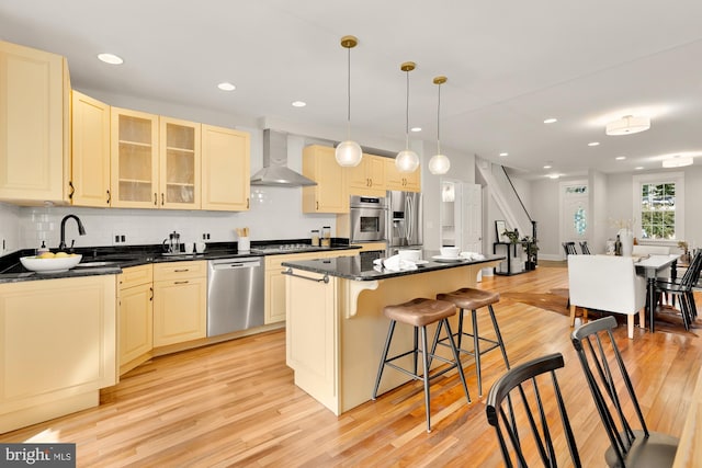 kitchen featuring sink, wall chimney range hood, decorative light fixtures, a kitchen island, and appliances with stainless steel finishes