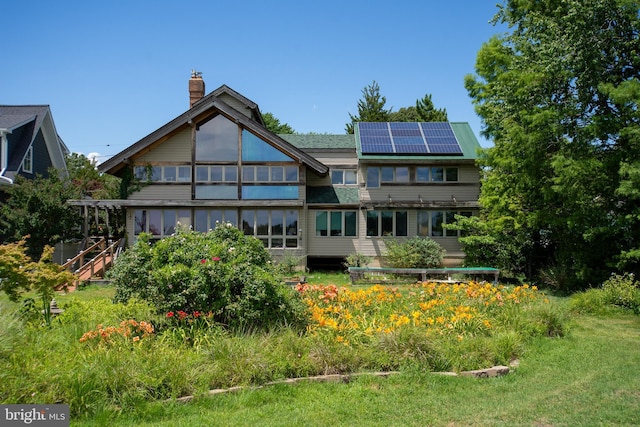 rear view of property with roof mounted solar panels and a chimney