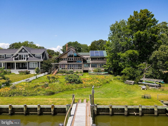 back of house with a lawn, solar panels, and a deck with water view