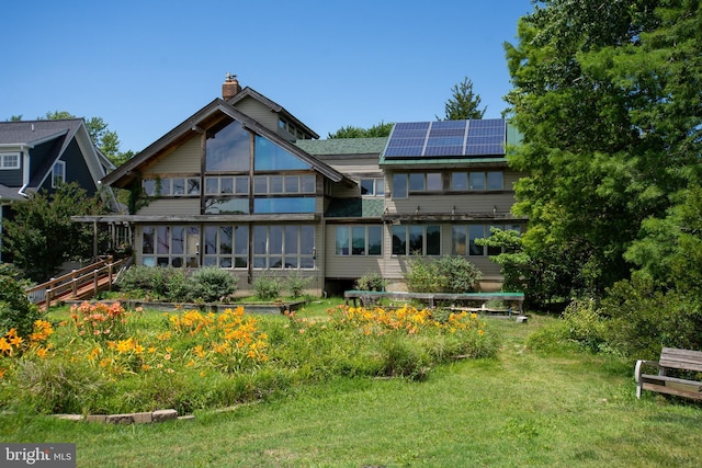 rear view of property featuring solar panels, a lawn, a sunroom, and a chimney