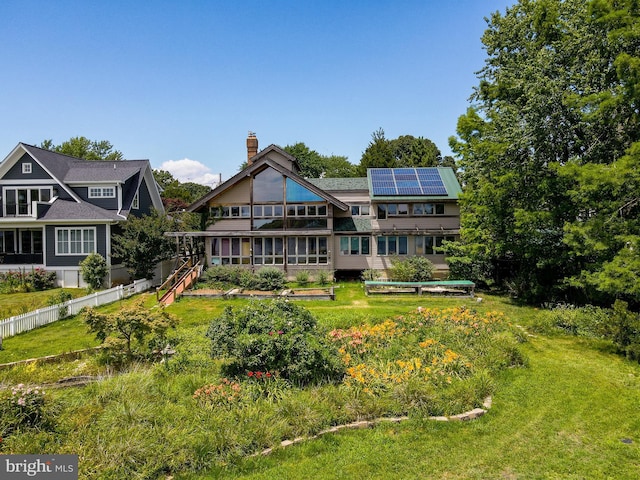 back of house featuring fence, solar panels, a chimney, and a lawn