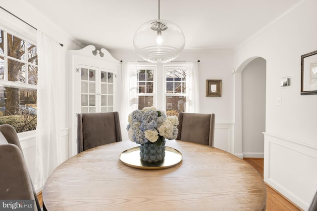 dining area featuring wood finished floors, a wainscoted wall, arched walkways, ornamental molding, and a decorative wall