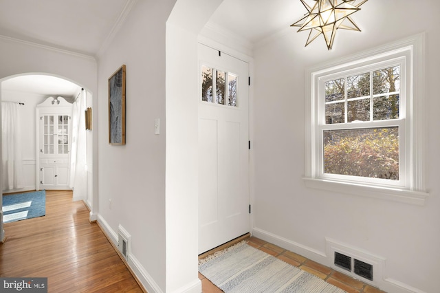 foyer with arched walkways, visible vents, baseboards, and ornamental molding