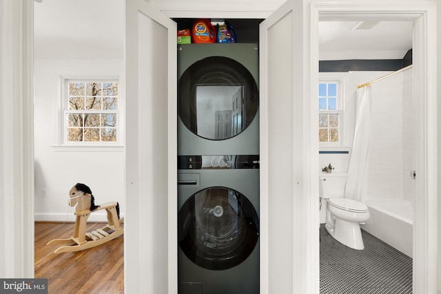 laundry area featuring wood finished floors, laundry area, and stacked washing maching and dryer