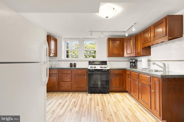 kitchen featuring light wood-style flooring, gas stove, freestanding refrigerator, and a sink