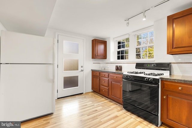 kitchen with tasteful backsplash, light wood-type flooring, range with gas stovetop, brown cabinets, and freestanding refrigerator